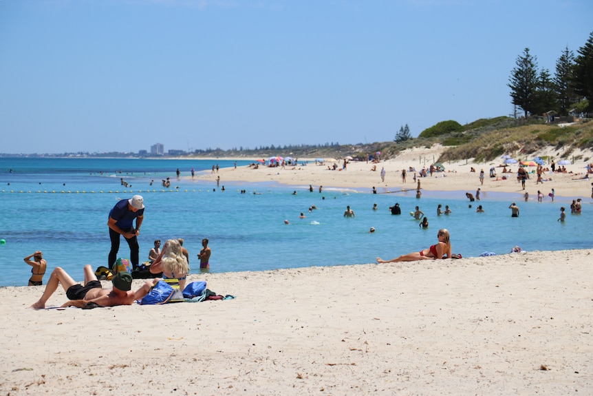 People sit on the banks of a beach while others swim in the water