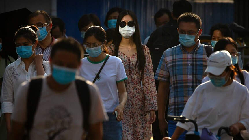 People wearing face masks wait to cross an intersection in Beijing, China.