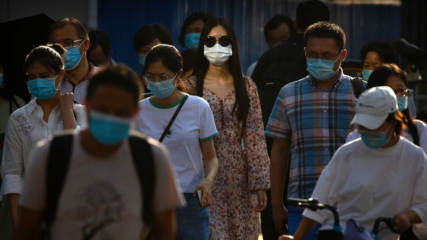 People wearing face masks wait to cross an intersection in Beijing, China.