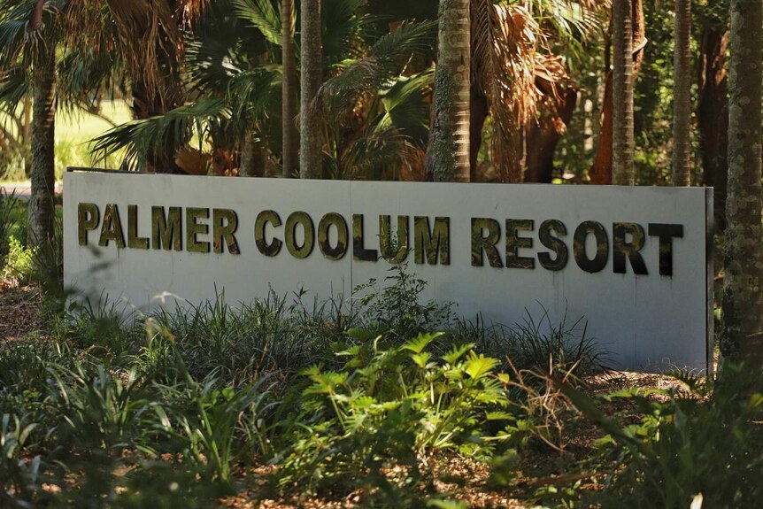 A sign saying 'Palmer Coolum Resort' with palm trees and shade behind it.