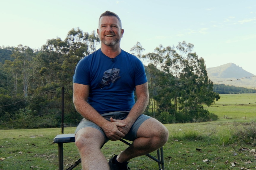 Innes sits on a bench in front of a lush, green view of his property