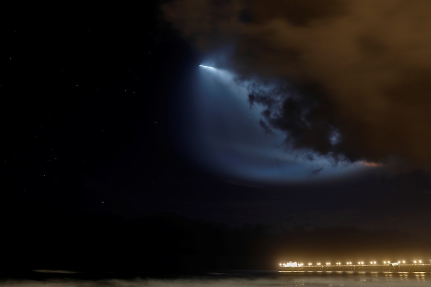 A rocket in the sky lights up the clouds.