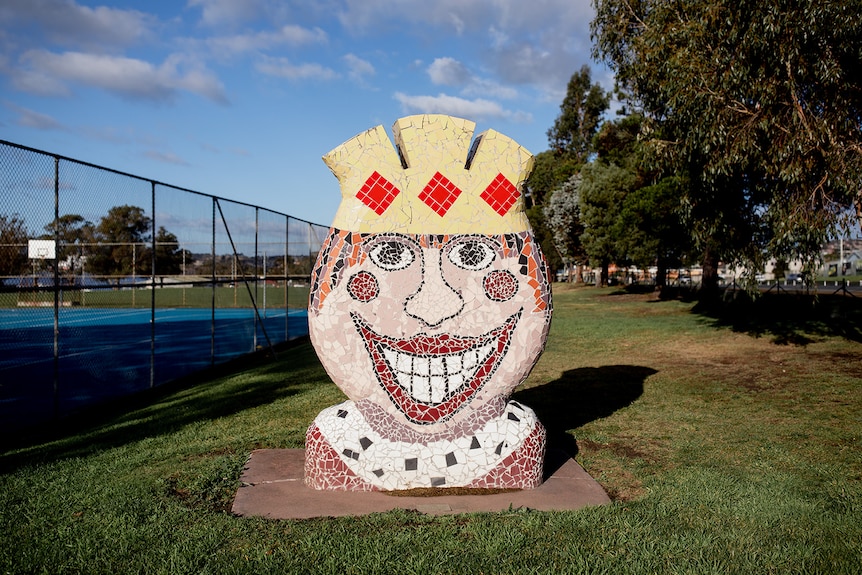 A coloured mosaic sculpture of a king with a huge smile, wearing a crown