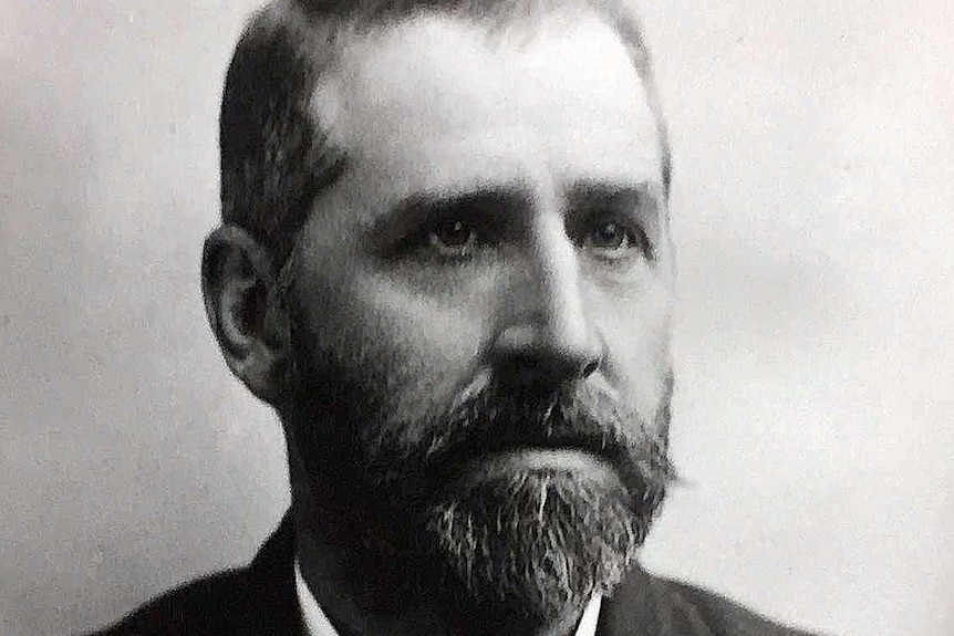 A black and white photo of a bearded man wearing a suit and tie.