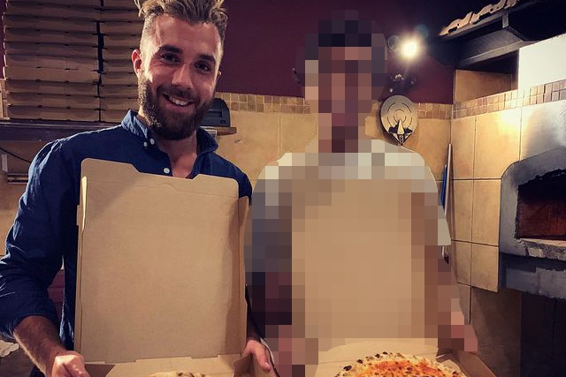 A close-up photo of a man holding a pizza box open standing next to another person.