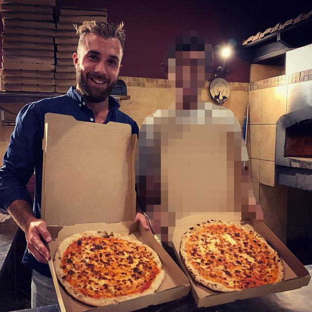 A close-up photo of a man holding a pizza box open standing next to another person.