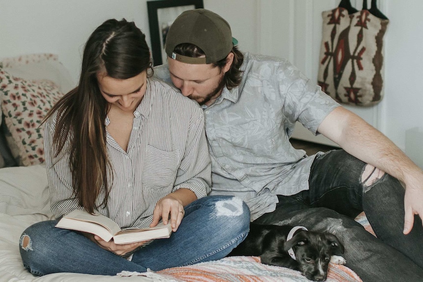 A couple sitting on a bed lovingly and looking at a baby names book, for a story about unique baby name popularity.