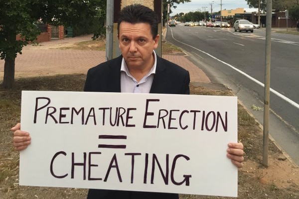 Nick Xenophon holds a sign with election poster on pole behind him.