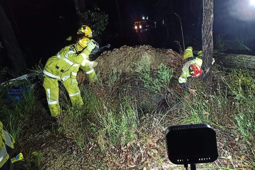 Firefighters stand around a hole in the ground lit up in the dark.