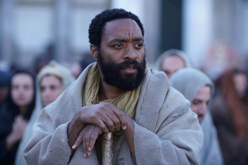 Midshot colour image from 2018 film Mary Magdalene of actor Chiwetel Ejiofor holding a cane and looking off into the distance.