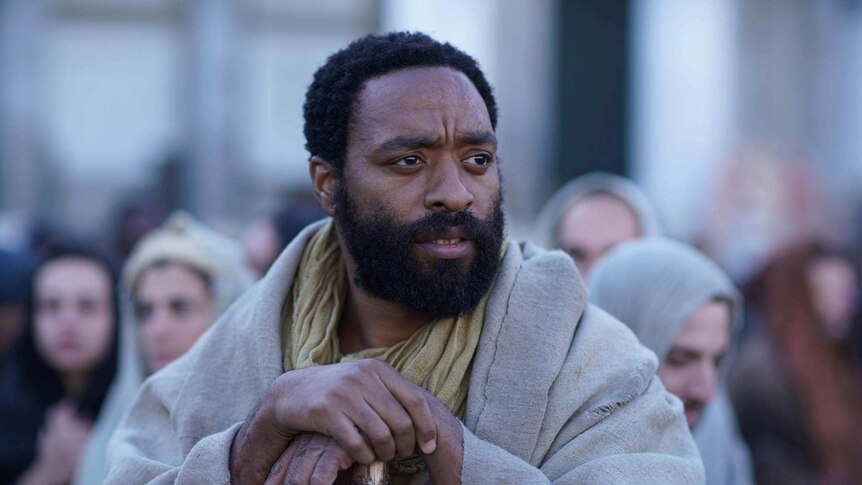 Midshot colour image from 2018 film Mary Magdalene of actor Chiwetel Ejiofor holding a cane and looking off into the distance.