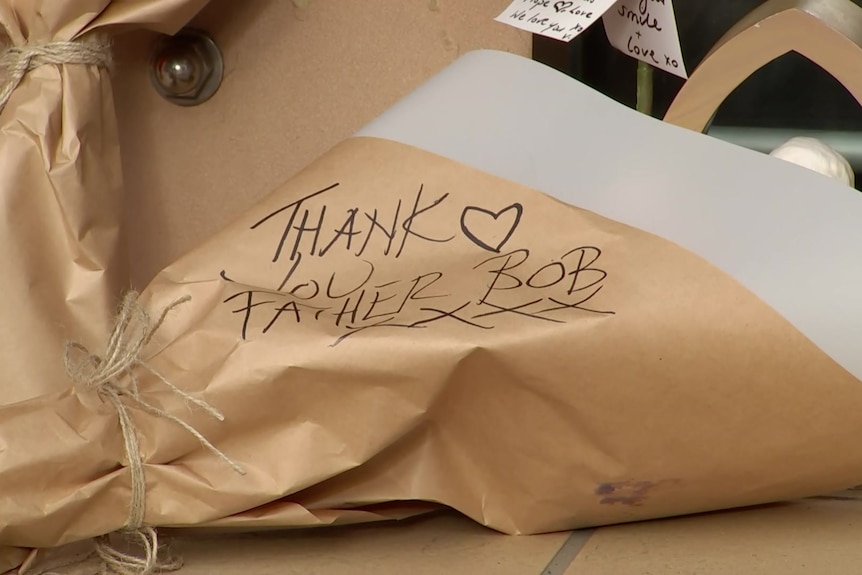 The words 'thank you Father Bob' written on the paper wrapping of a bouquet of flowers.