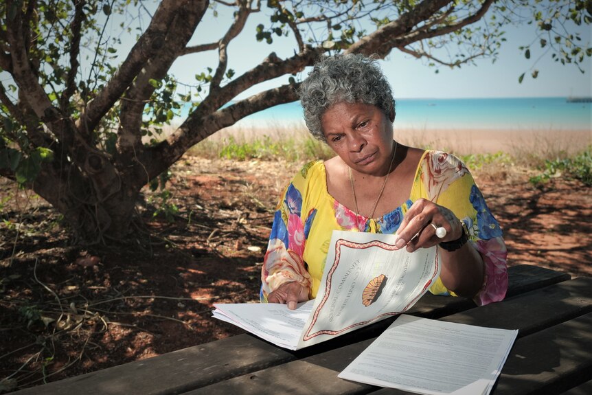 Vennessa Poelina looks over her ACBF certificates with the beach in the background.