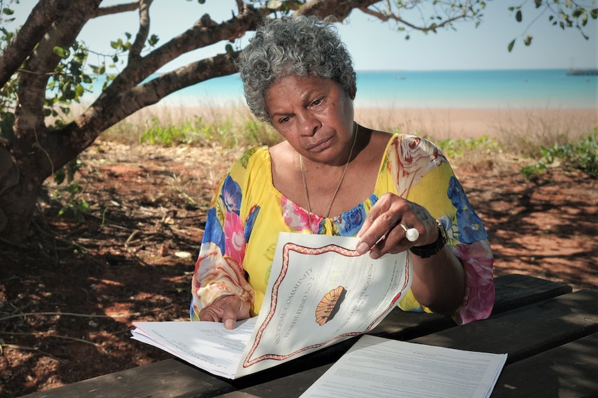 Vennessa Poelina looks over her ACBF certificates with the beach in the background.