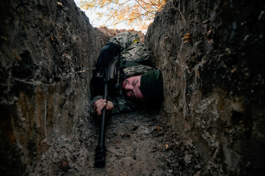 Мужчина в военной форме лежит в узкой яме
