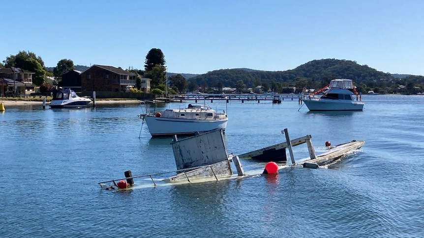 Old wooden boat is half emersed in water, still on its mooring at Empire Bay. 