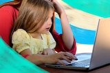 Young girl sitting on her mother's lap as the mum worked on a laptop.