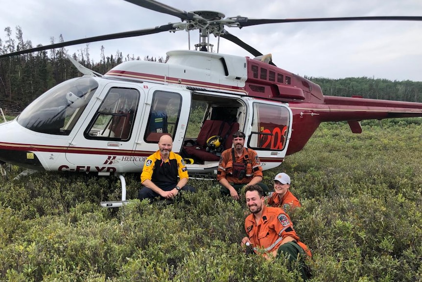 A helicopter with four firefighters sitting in the grass in front of it