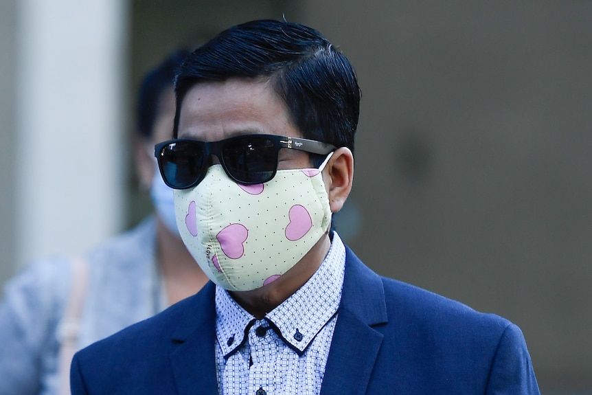 My Ut Trinh wears sunglasses and a face mask with pink hearts, in a blue suit.