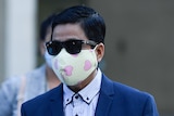 My Ut Trinh wears sunglasses and a face mask with pink hearts, in a blue suit.