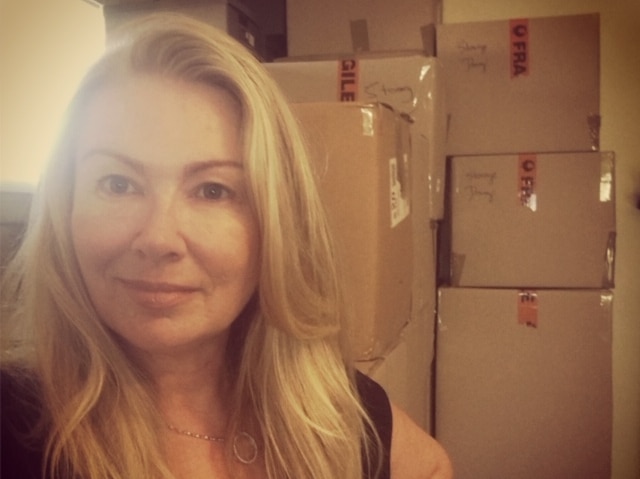 A woman with long blonde hair sitting in front of a pile of moving boxes