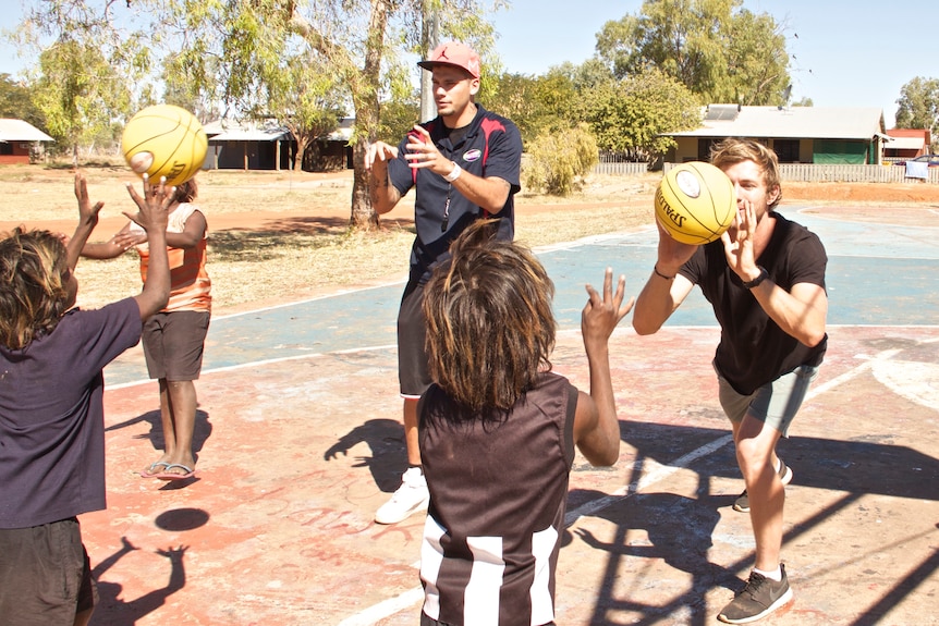 Kids throwing basketballs to the adult teachers.