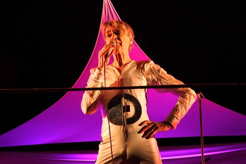 Jeff Duff, dressed in a style similar to David Bowie, performs in front of a pink tent.
