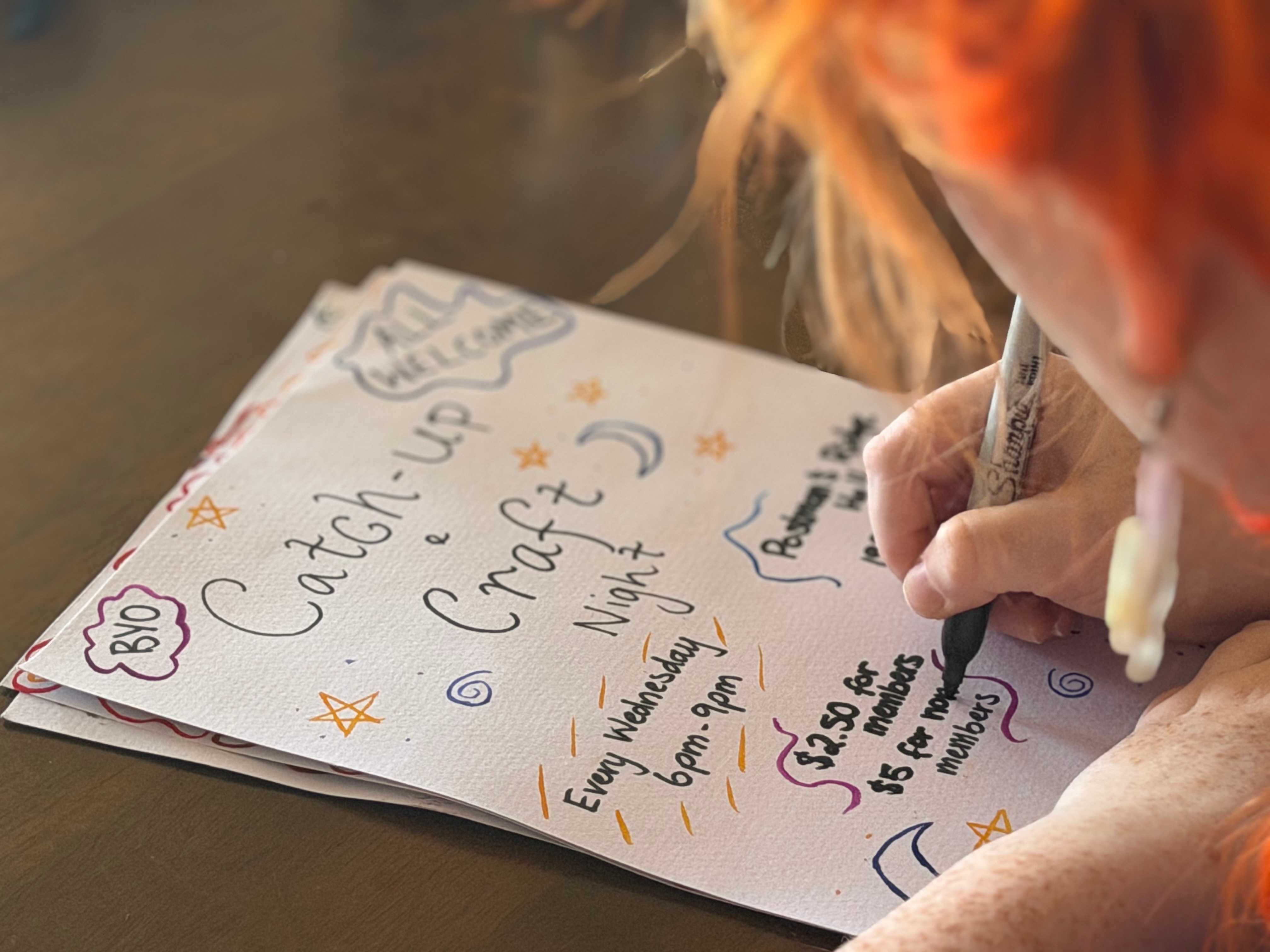 A young woman draws a poster by hand with a coloured pen.