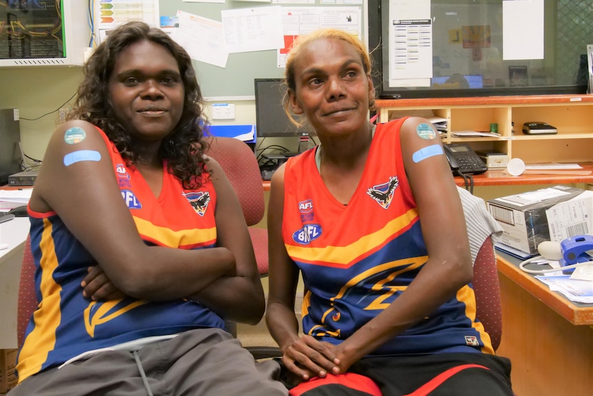 Two Aboriginal women smile at the camera with bandaids on arms after 
