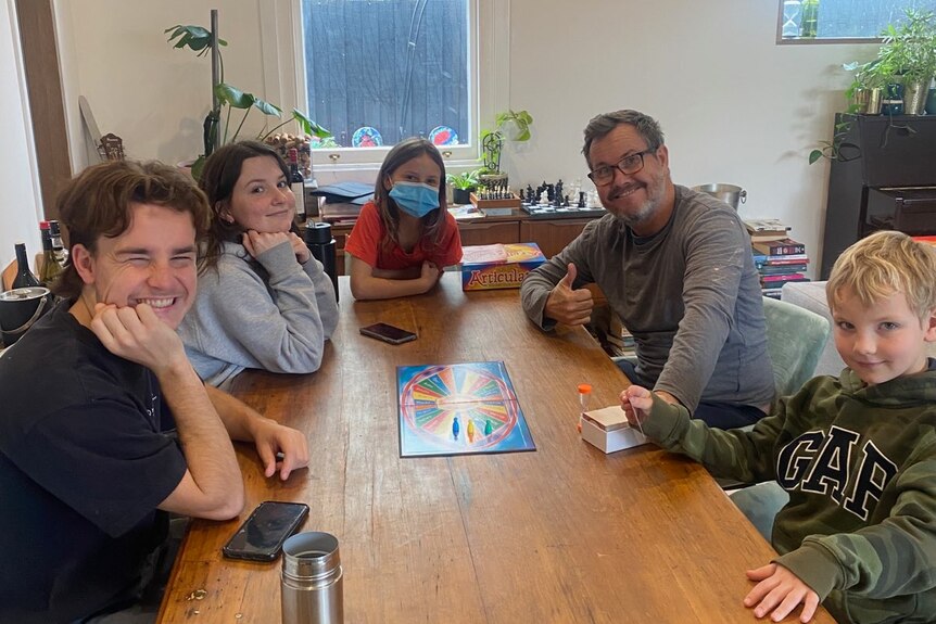 Five family members sit on a table with a board game in the centre