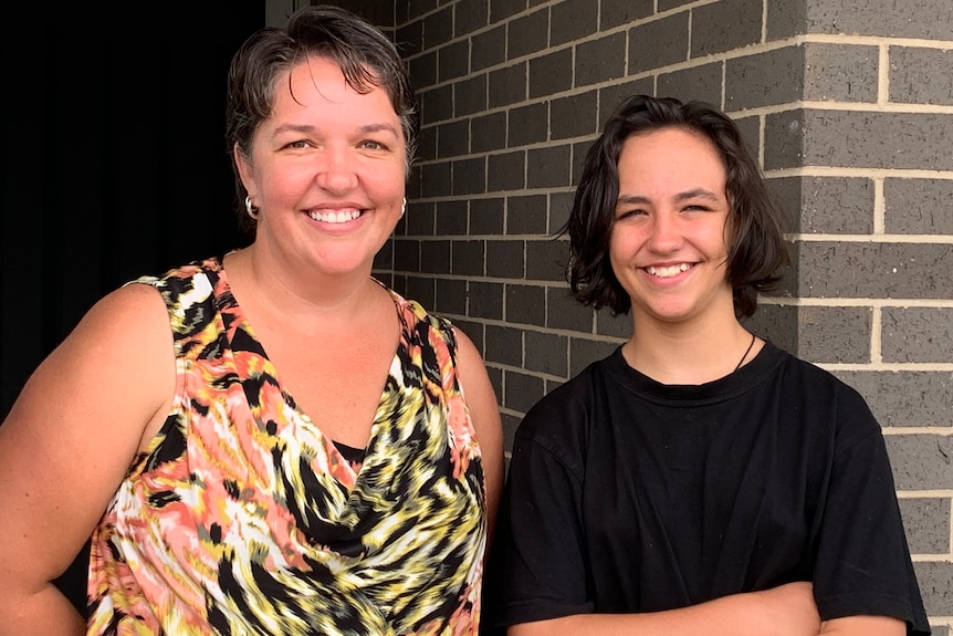 A mother and daughter smiling and standing side by side