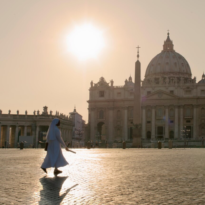 nun dressed in white walks in front of the St Peter's Basilica at the Vatican, on a sunny day