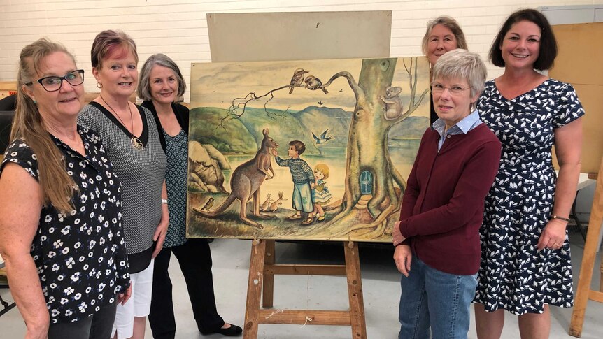A group of women in an art gallery standing around a Pixie O'Harris painting.