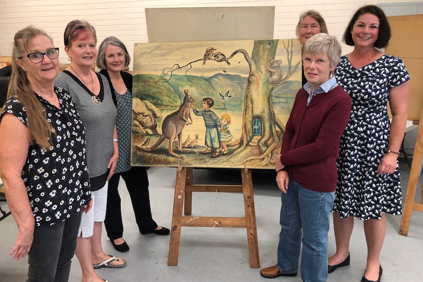 A group of women in an art gallery standing around a Pixie O'Harris painting.