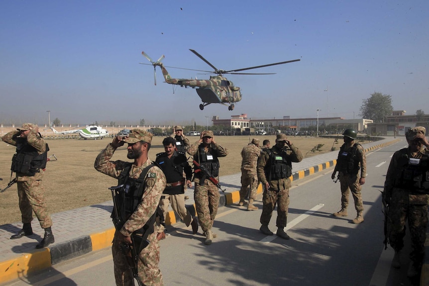 Soldiers holds their caps as a helicopter flies past during an operation near Bacha Khan University in Pakistan.