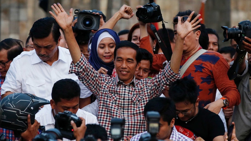 A man greets a large crowd and photographers.