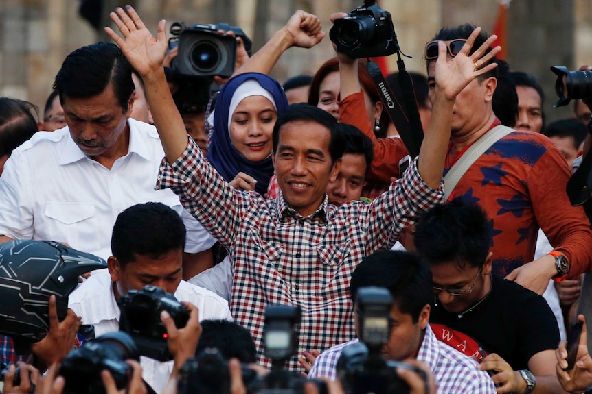 A man greets a large crowd and photographers.