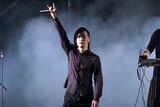 Freddy Lim gestures the sign of the horns while holing a microphone on stage