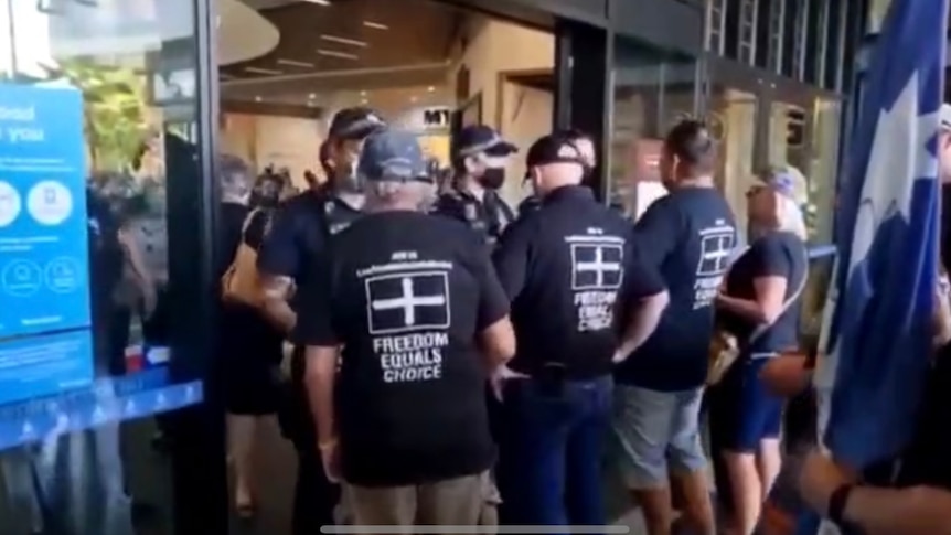 Police block a shopping centre entry-way to a group of men 