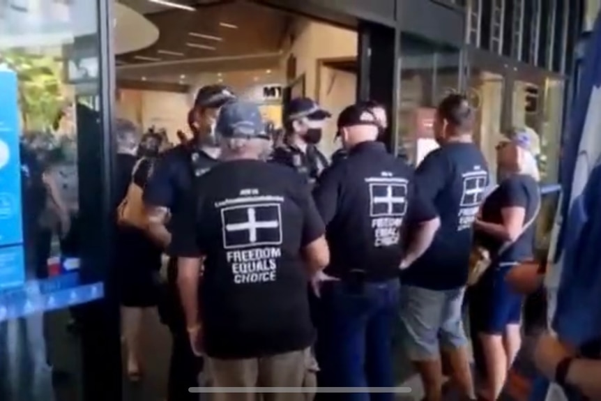 Police block the entry to a shopping centre, facing off with men in T-shirts emblazoned with the Eureka flag.