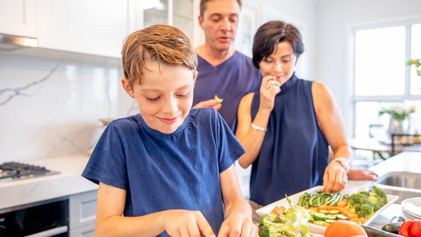 Mum, Dad and their two young boys chopping and preparing vegetables for a meal inside their luxury home