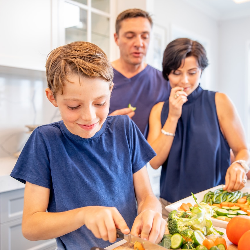 Mum, Dad and their two young boys chopping and preparing vegetables for a meal inside their luxury home