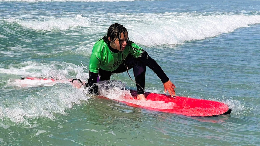 A school-aged child on a small wave preparing to stand on a surf board