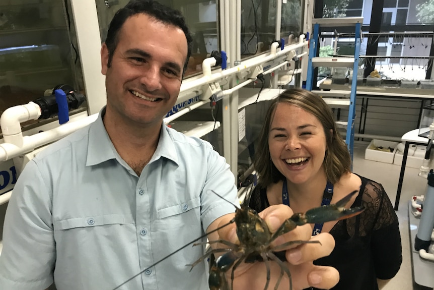Tomer Ventura and Jennie Chandler smiling as Tomer holds up a red claw cray fish to the camera.