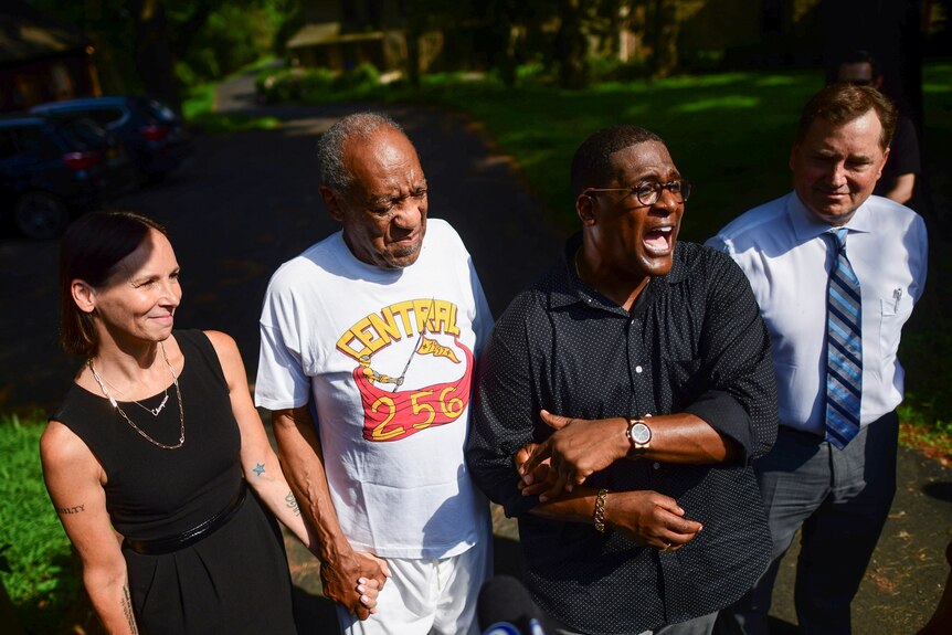 Bill Cosby standing with a woman on one side and two men on the other. 