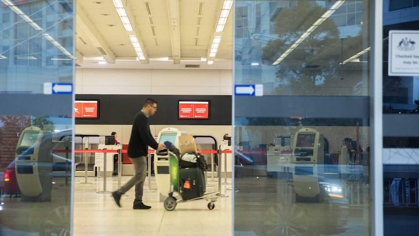 A man walks across an empty check-in area with a trolley bags on a trolley