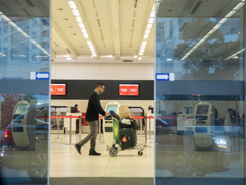 A man walks across an empty check-in area with a trolley bags on a trolley