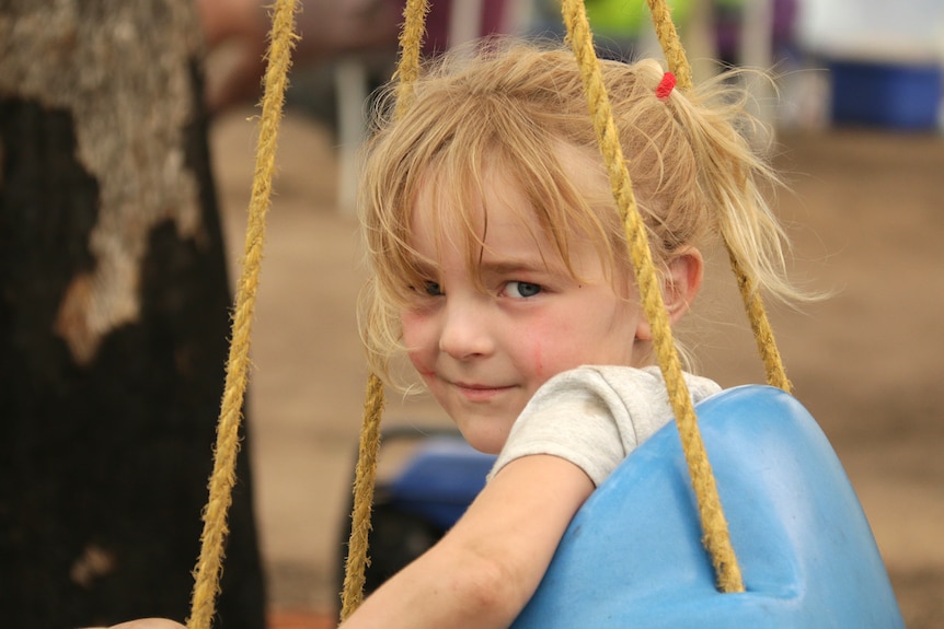 Five year old Layla sits on a swing in her garden, looking at the camera