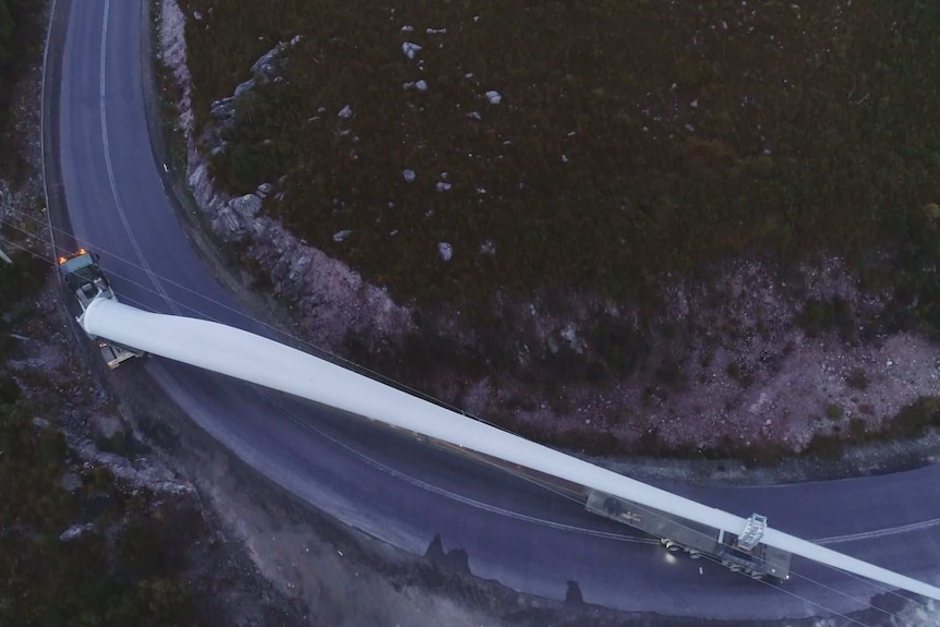 A 70m long windfarm blade is moved by truck around a tight mountain bend