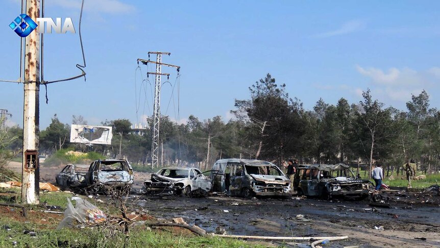 Charred and damaged cars sit on the road.